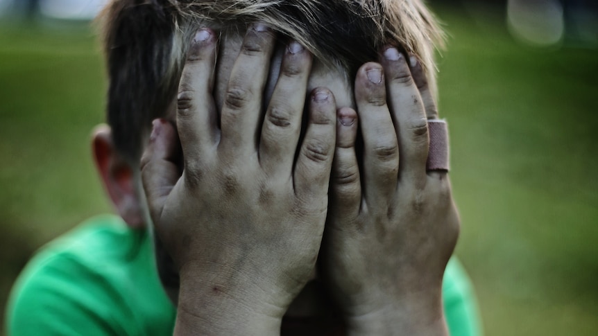 A small boy covering his face with both hands while throwing a tantrum.