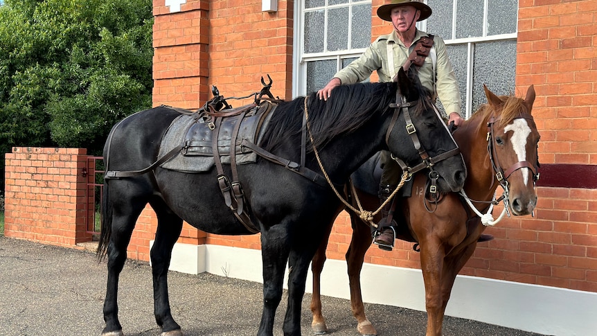 A man riding a brown horse next to a black horse