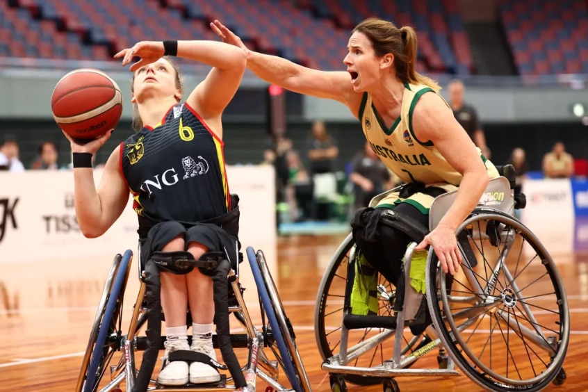 Two female wheelchair basketballers are on the court, one is preparing to shoot, the other is defending.