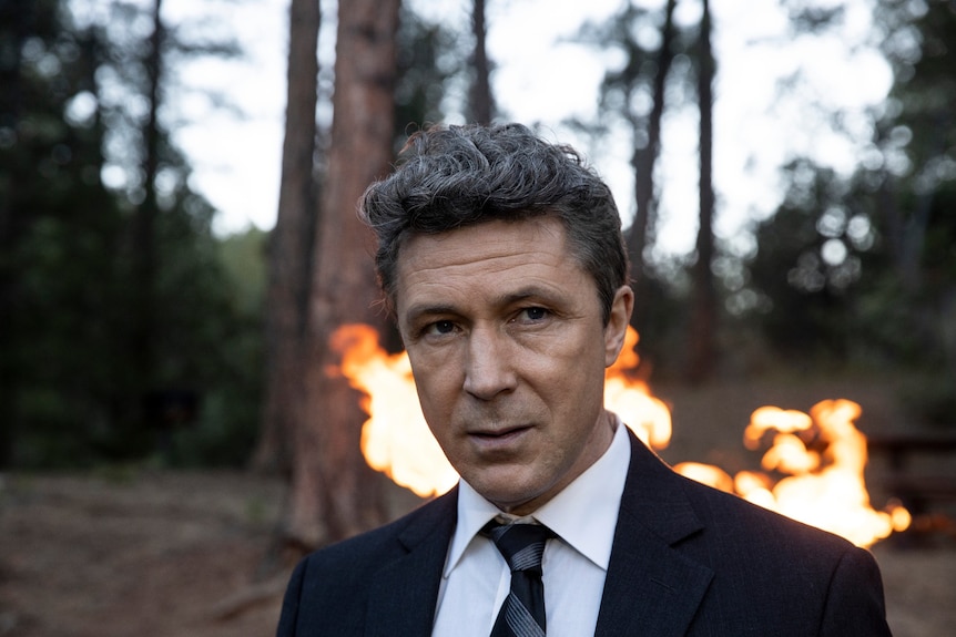 Film still of Aidan Gillen as Jack standing in front of a forest fire in Those Who Wish Me Dead