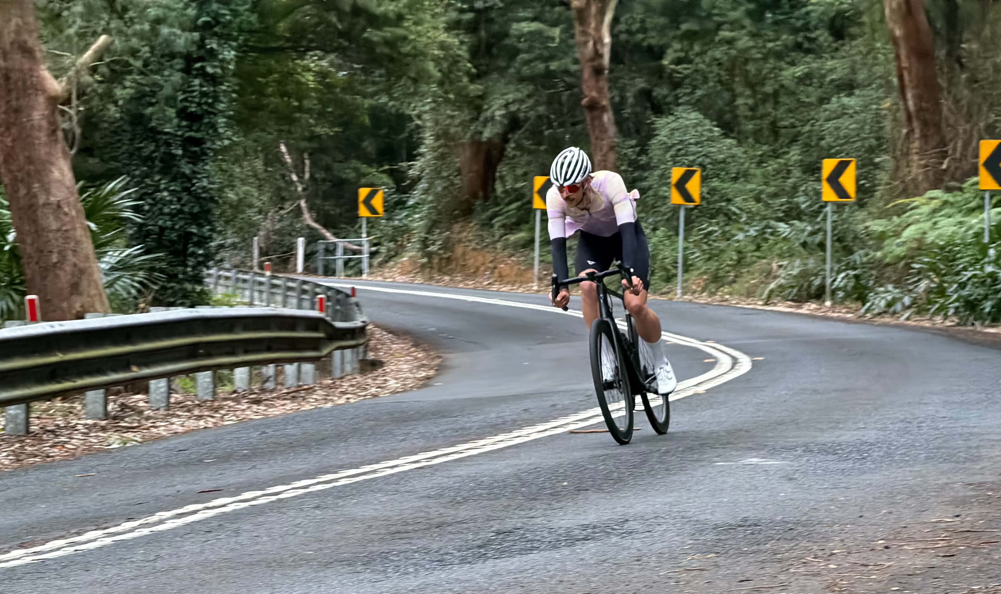 A young man riding a road bicycle down a mountain with green shrubbery in the background.