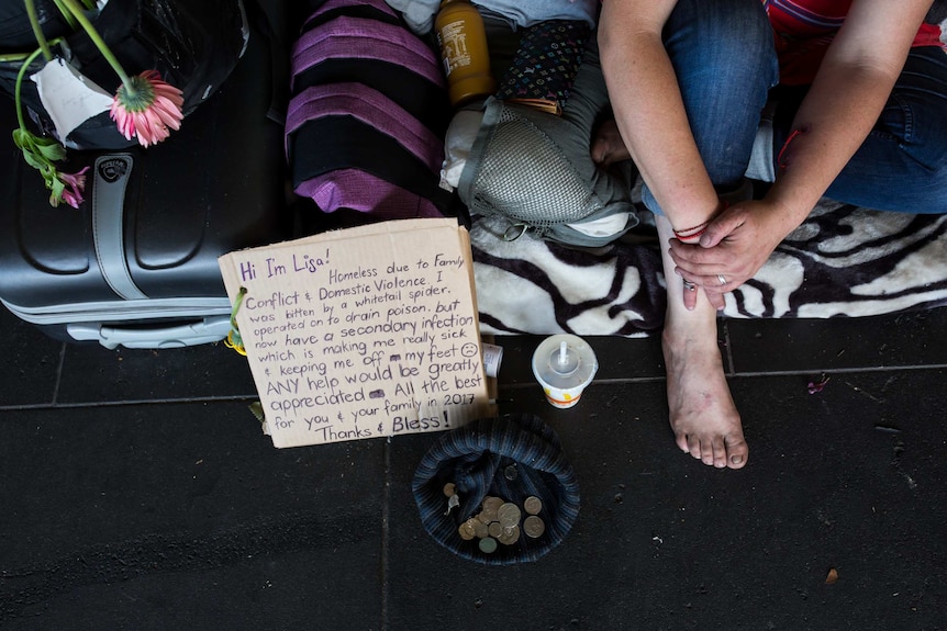 A woman sits with a sign asking for money in Melbourne's CBD. She has no shoes and has a hat with coins.