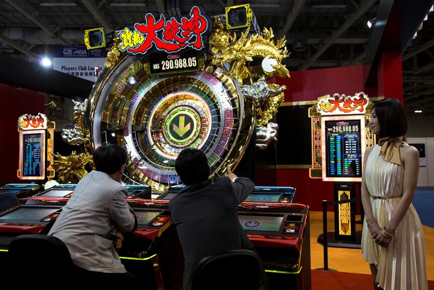 Two men play at poker machines while a woman in a gold dress looks on