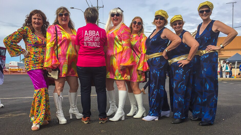 A group of women in flares and mini dresses with one with her back to the camera and a shirt saying ABBA Great day in Trundle