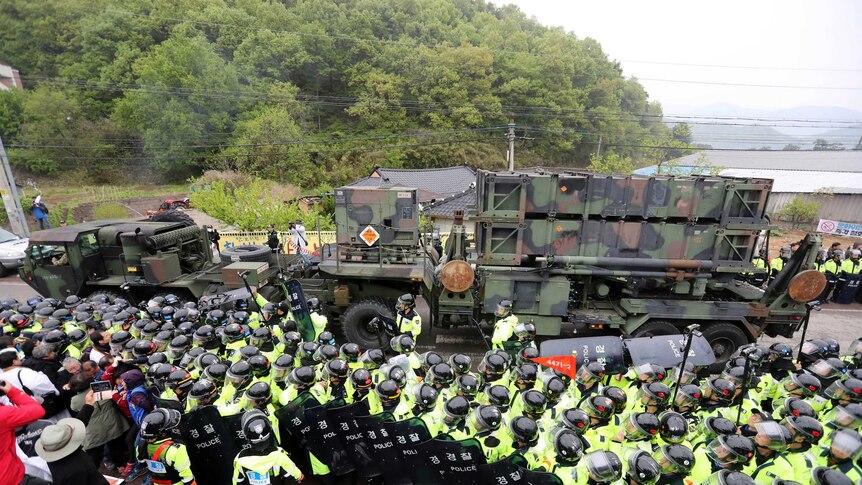 Several policemen stand between protesters and a military vehicle.