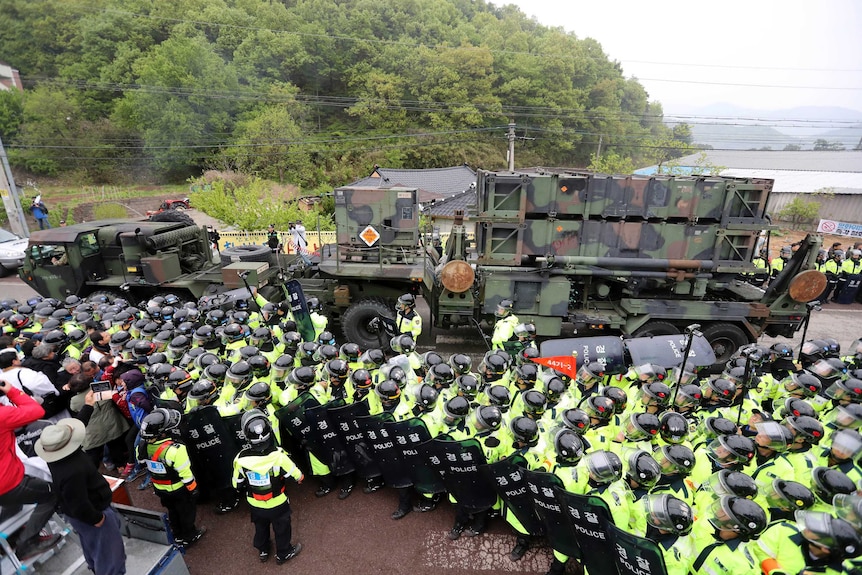 Several policemen stand between protesters and a military vehicle.