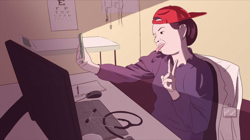 a female doctor at her desk taking a selfie with a cap on backwards and doing the peace sign