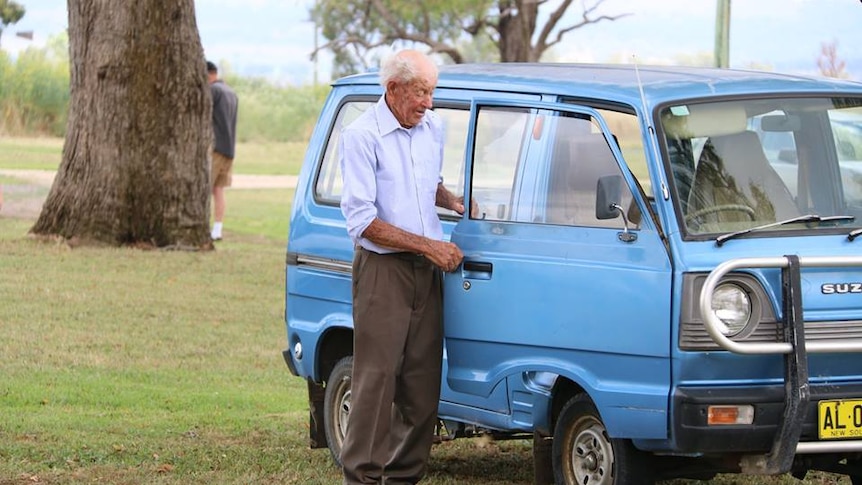 Elderly man standing next to blue van.