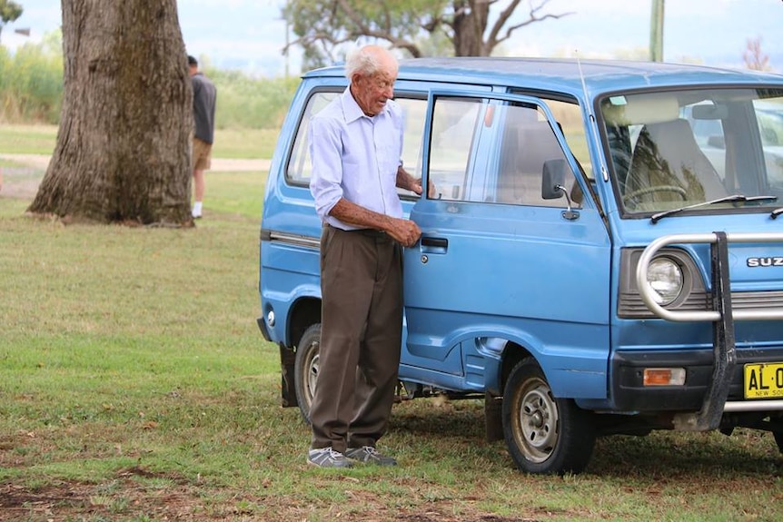 Elderly man standing next to blue van.