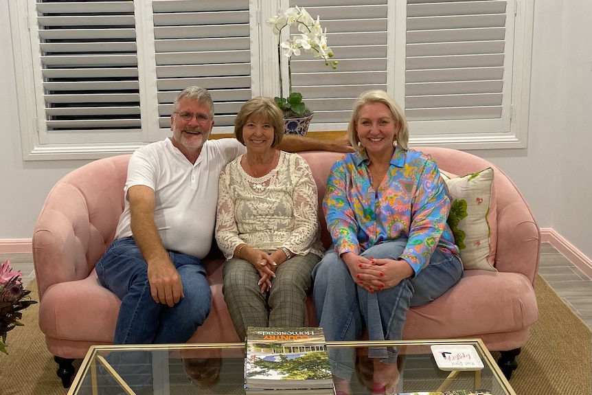Three people sitting on a lounge in a room, all smiling at the camera