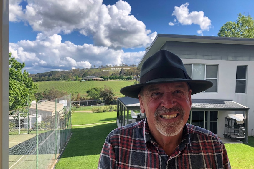 A smiling man wearing a hat with Mount Panorama in the far distance.