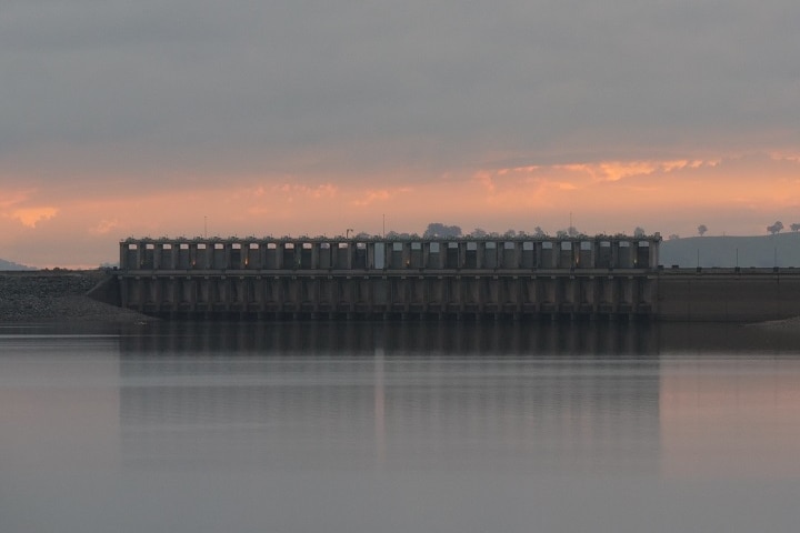 A large dam with the sun low in the sky behind it.