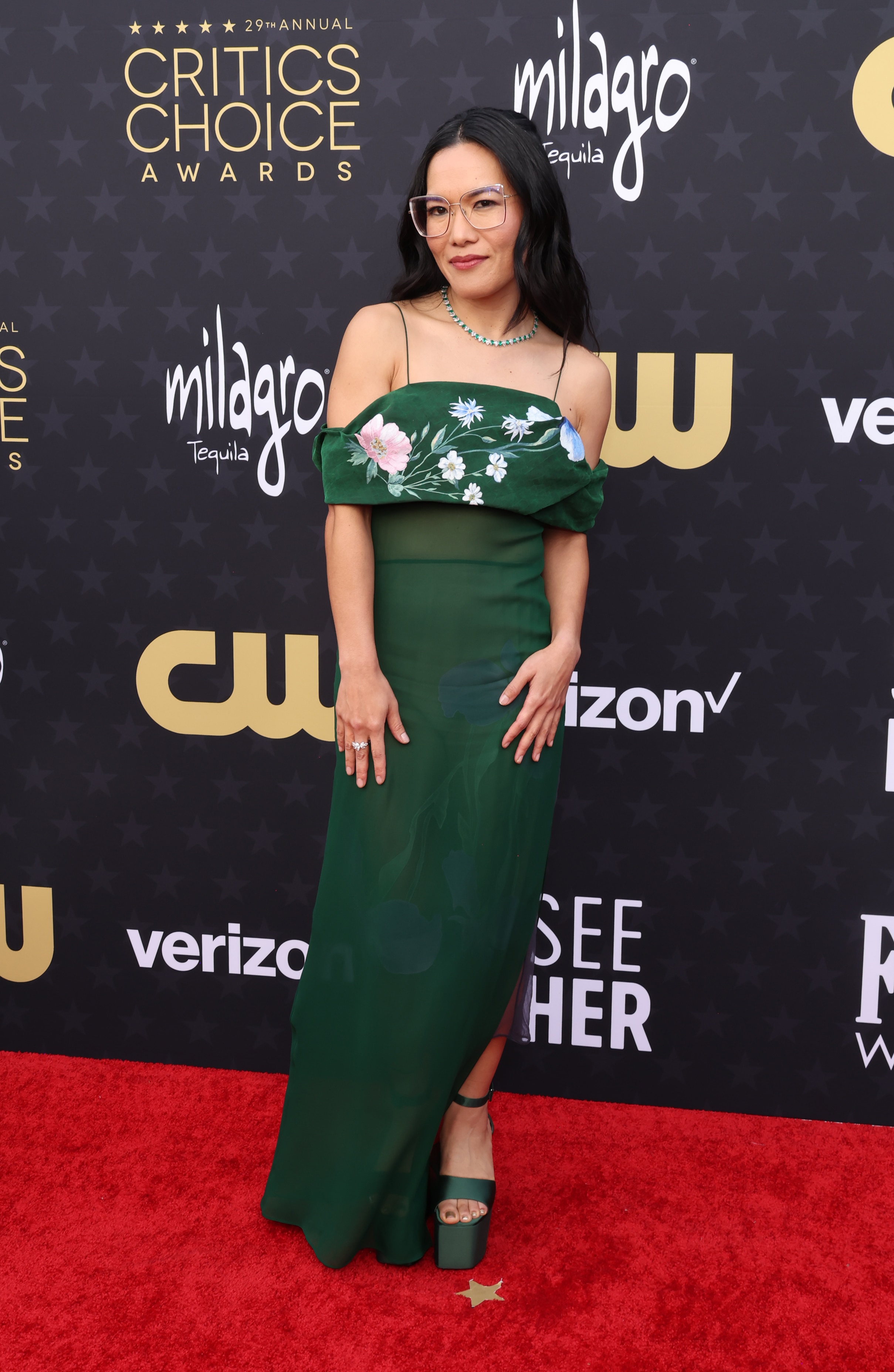 Ali Wong wearing a bottle green strappy dress with floral detailing and big platform shoes