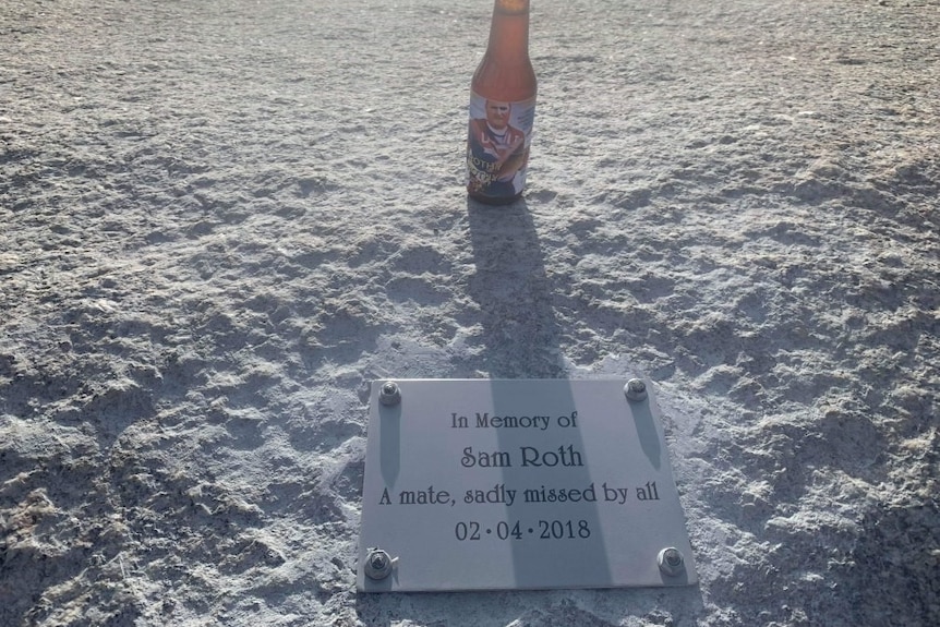 A memorial plaque on a rock overlooking the ocean next to a beer bottle.