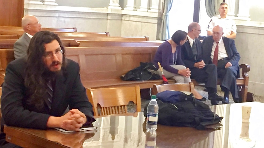 Michael Rotondo sits in a courtroom during an eviction proceeding while his parents confer with their lawyer behind him.