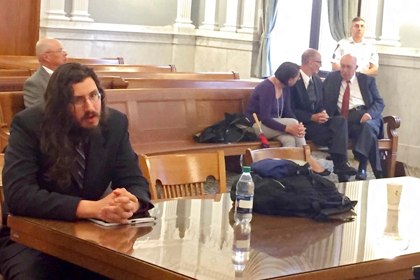 Michael Rotondo sits in a courtroom during an eviction proceeding while his parents confer with their lawyer behind him.