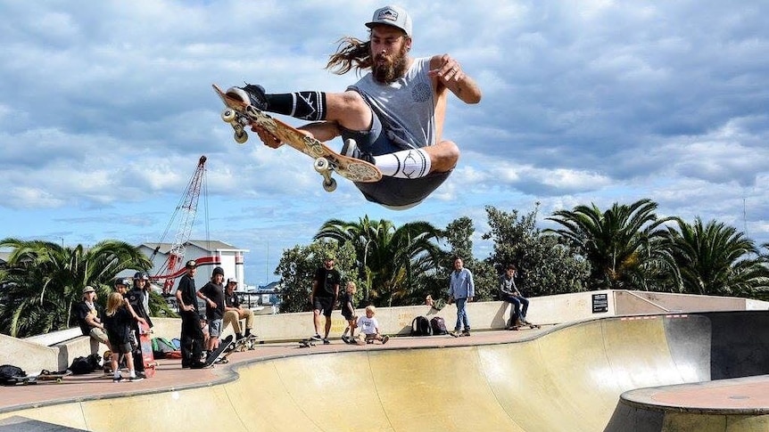 A skater gets some air at a skate park as other skaters look on.