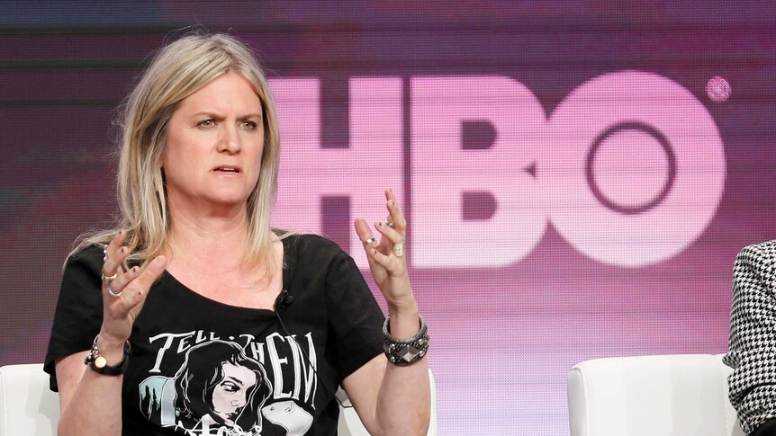 A woman talks with her hands in the air with an HBO logo in the background