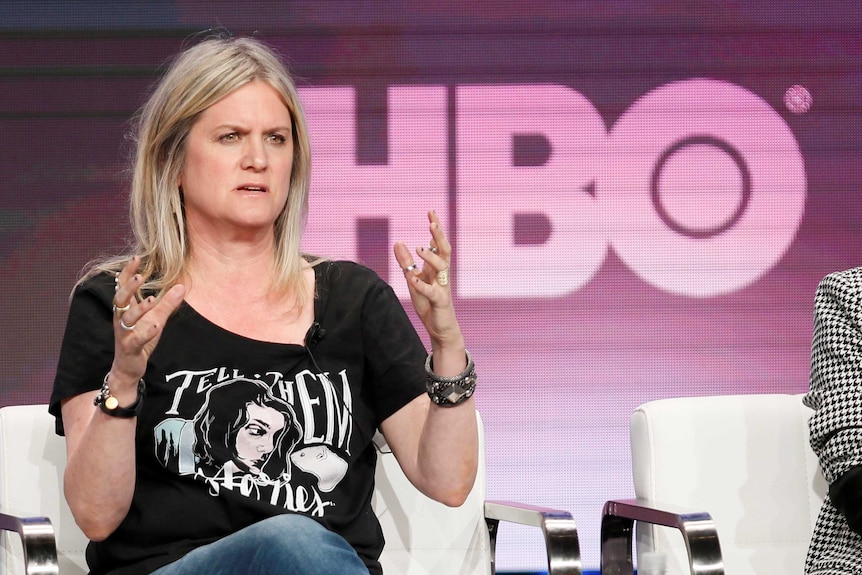 A woman talks with her hands in the air with an HBO logo in the background
