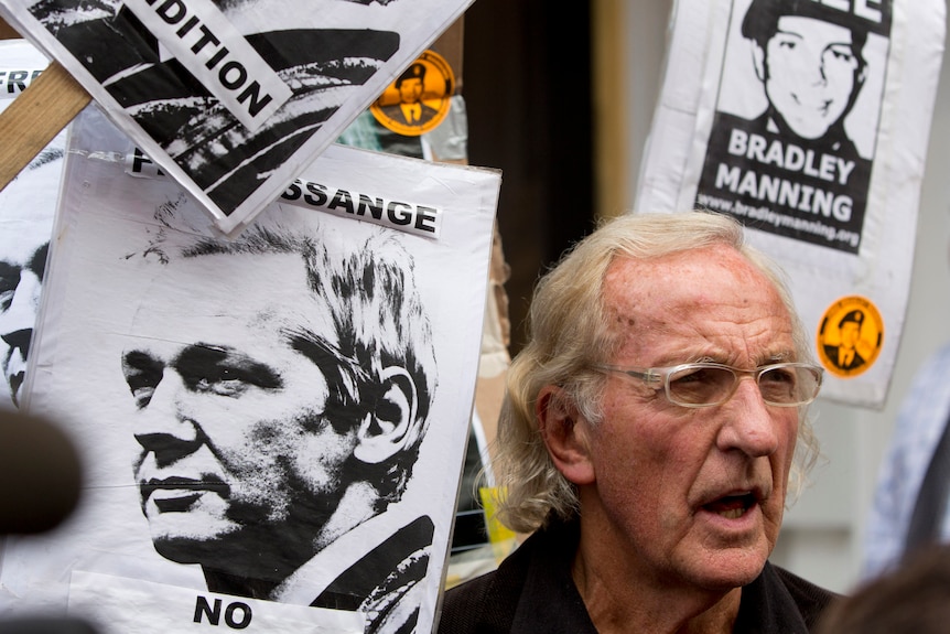 An olde rman with blond hair stands amongst a sea of black and white posters of Julian Assange and Bradley Manning.
