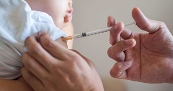 An adult hand holds a needle to the arm of a small child, who has a restful, neutral expression.