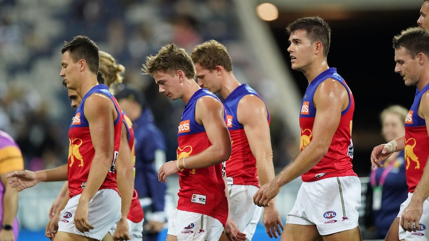 A group of dejected AFL players walk off the field.
