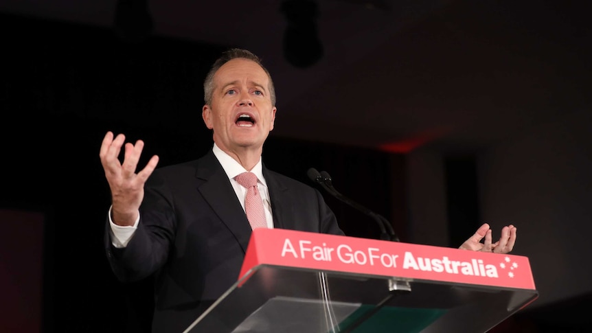 Bill Shorten holds his arms out wide as he speaks at a lectern.