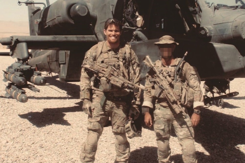 Two men stand in front of a helicopter in a war setting