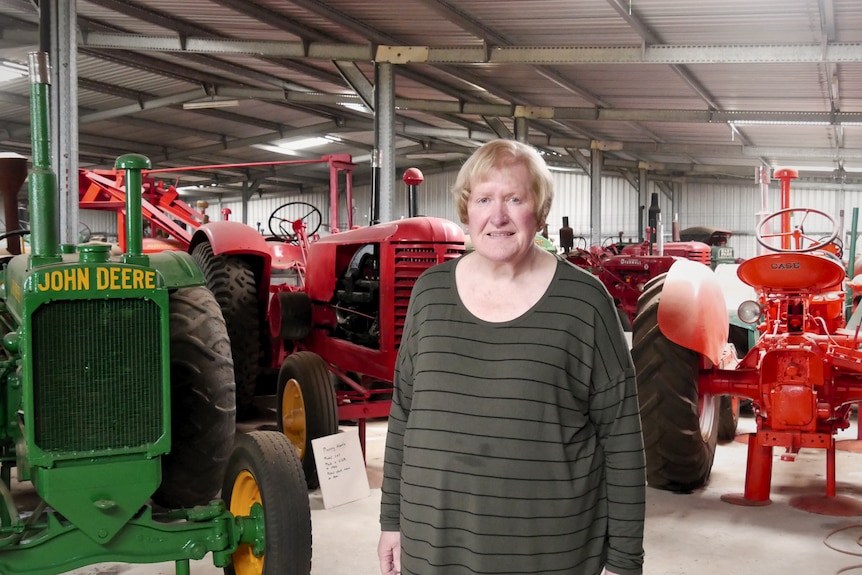 A woman stands in a shed full of vintage tractors
