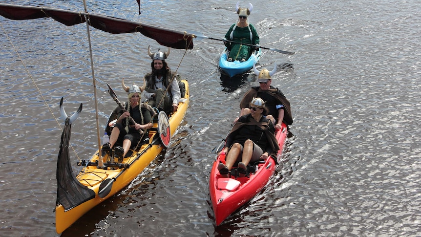 People dressed as vikings with horned helmets float in kayaks on river