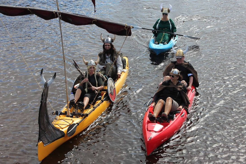 People dressed as vikings with horned helmets float in kayaks on river