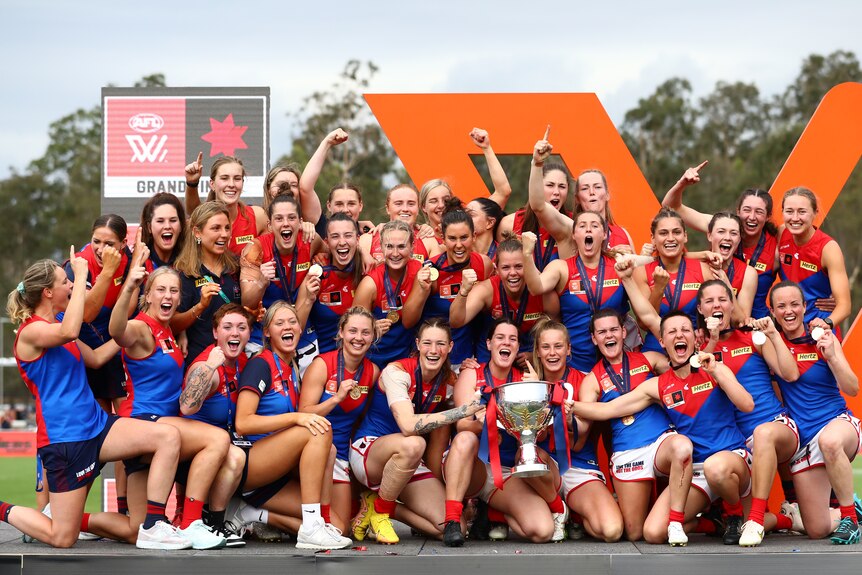 An AFLW team standing on the podium, holding the premiership cup, celebrating