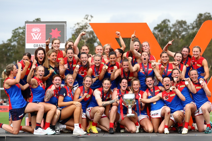 An AFLW team standing on the podium, holding the premiership cup, celebrating