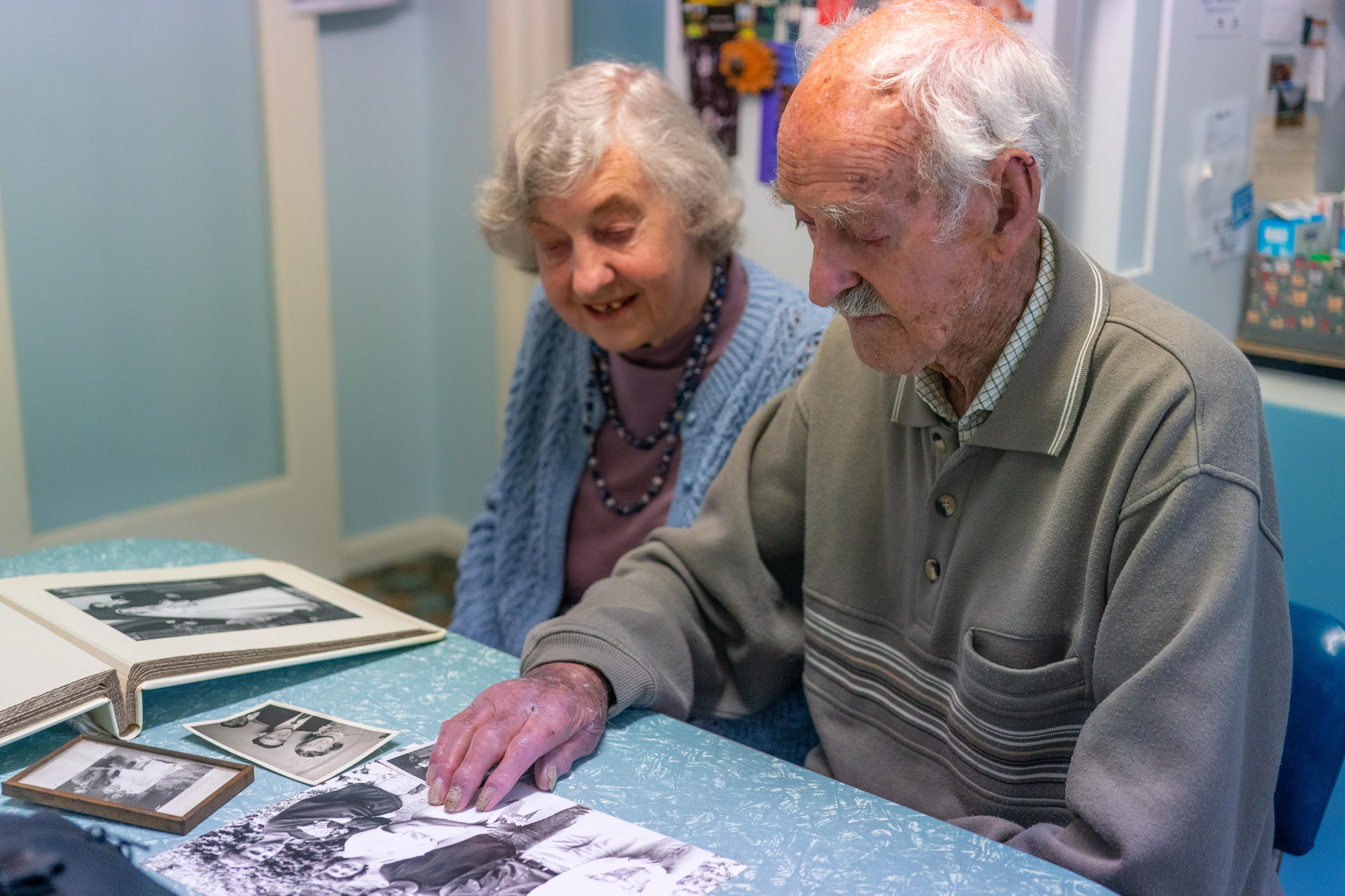 A man and women sitting at a table, looking at black and white photographs. 