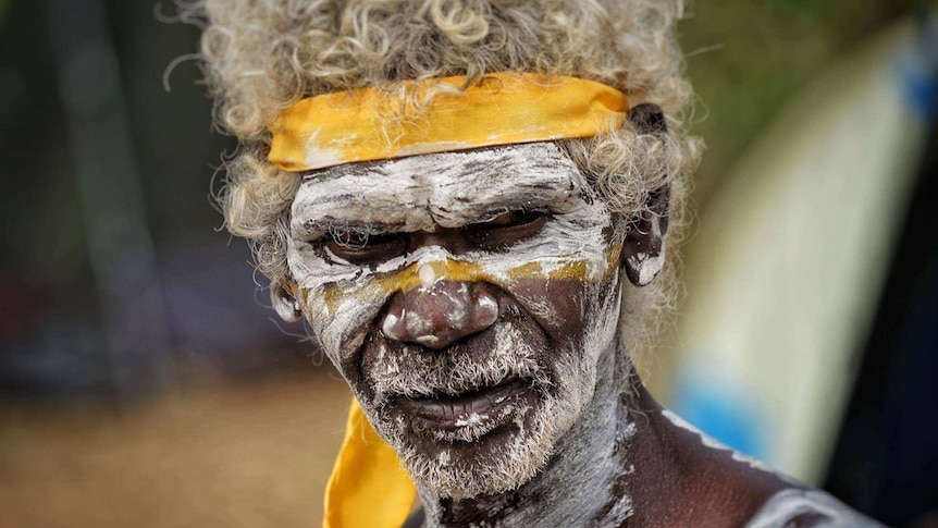 Aboriginal man Eddie William Gumbula stands with his face and chest painted white as he performs at the Garma Festival.