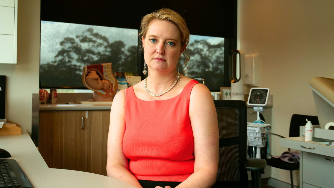 a woman sitting in a doctor office, she has short blonde hair, a pink singlet on 