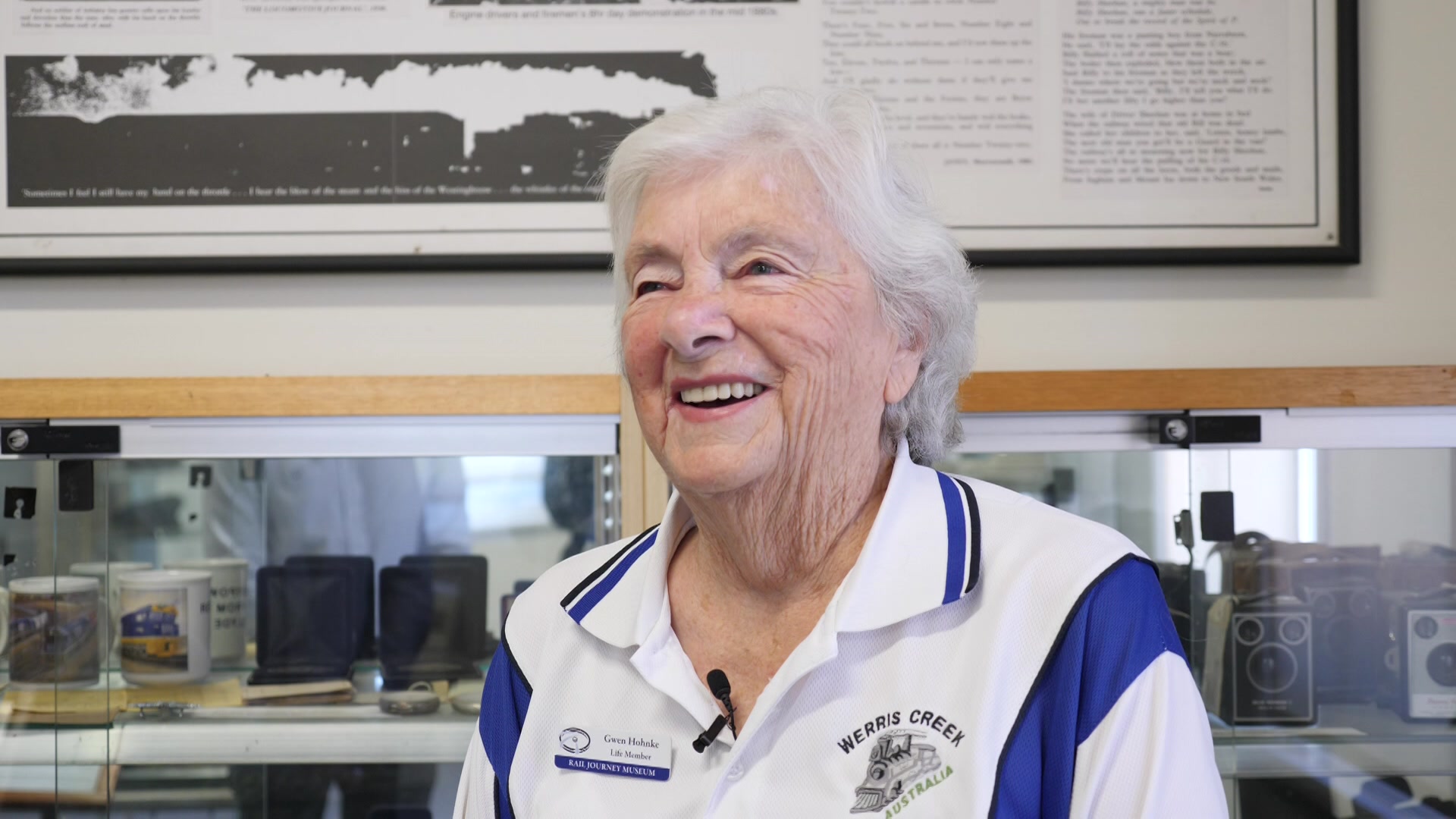 Uma mulher vestindo uma camisa pólo azul e branca sorri.