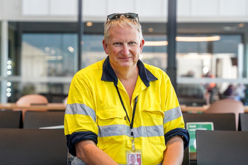 A man in a warning shirt sits on a chair in the airport terminal.