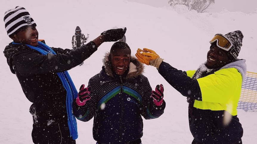 Three young boys from refugee backgrounds catch snow in their hands