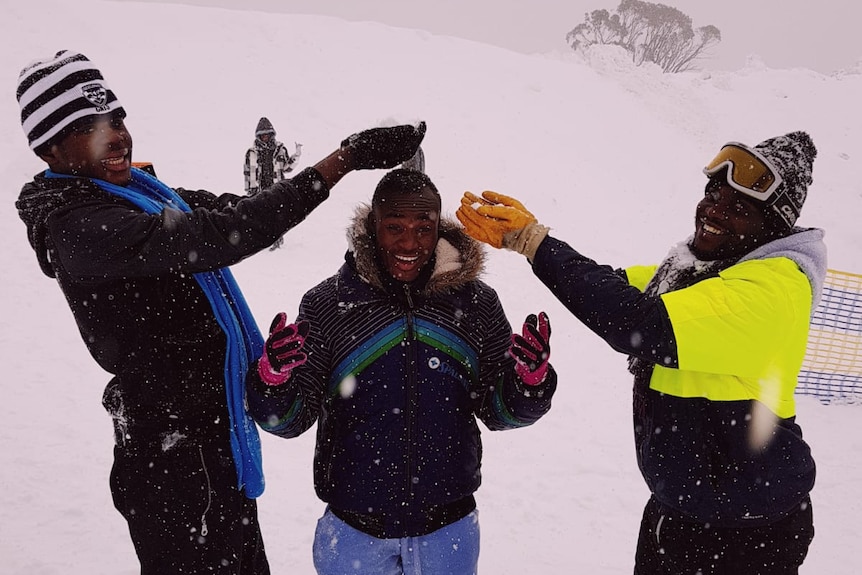 Three young boys from refugee backgrounds catch snow in their hands