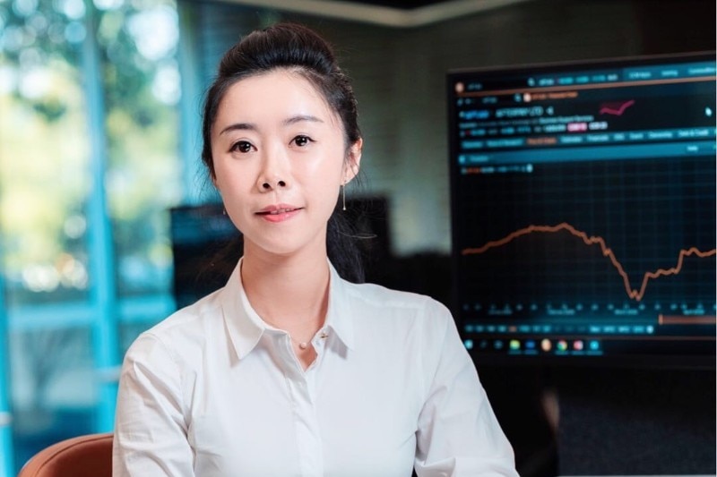 A woman seated at a desk, with a Bloomberg terminal behind her