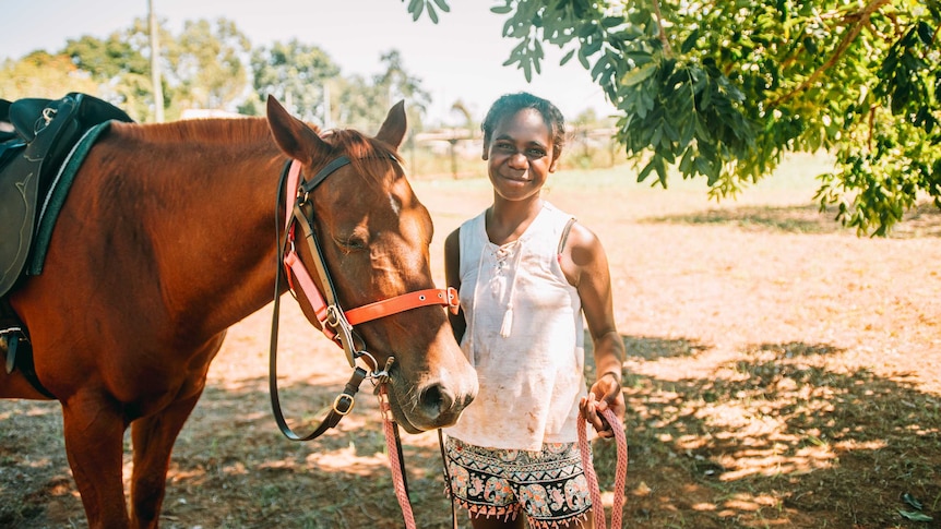 Doomadgee State School student Jahlee Sambo holding a horses bridle, and smiling at the camera.