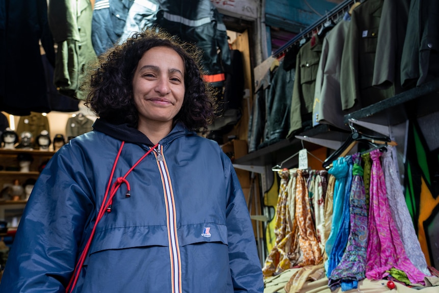 A woman with dark curly hair smiles while standing in a clothes store.