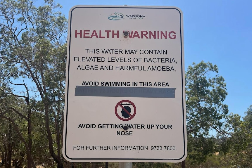 A sign outside a dam saying, 'health warning, this water may contain elevated levels of bacteria, algae and harmful amoeba'