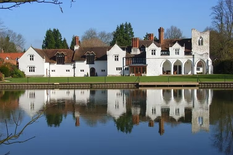 A sprawling white mansion set by water, with a reflection of the building in it