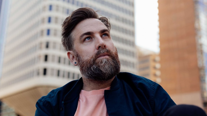 A side view of a bearded Josh Pyke wearing blue and peach