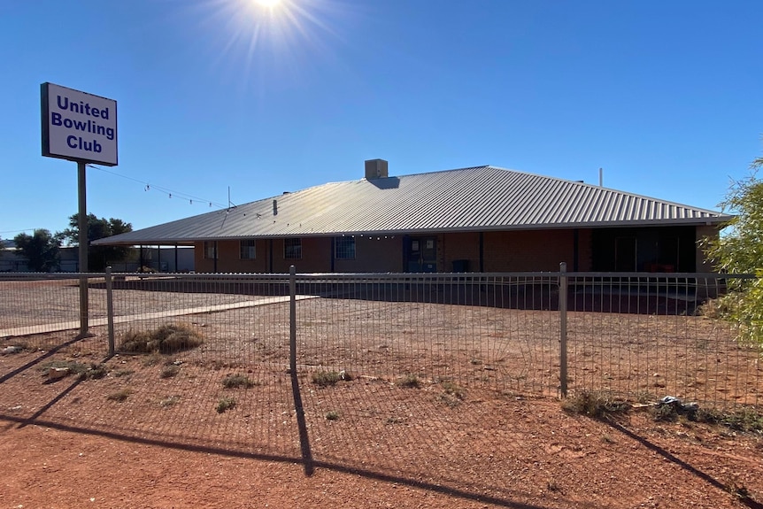 A low-set building with a sign saying "United Bowling Club" surrounded by red dirt