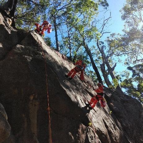 People in SES uniforms abseiling down a cliff face.