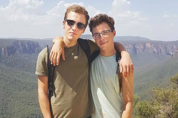 two men with arms around each other's shoulders with mountains in background