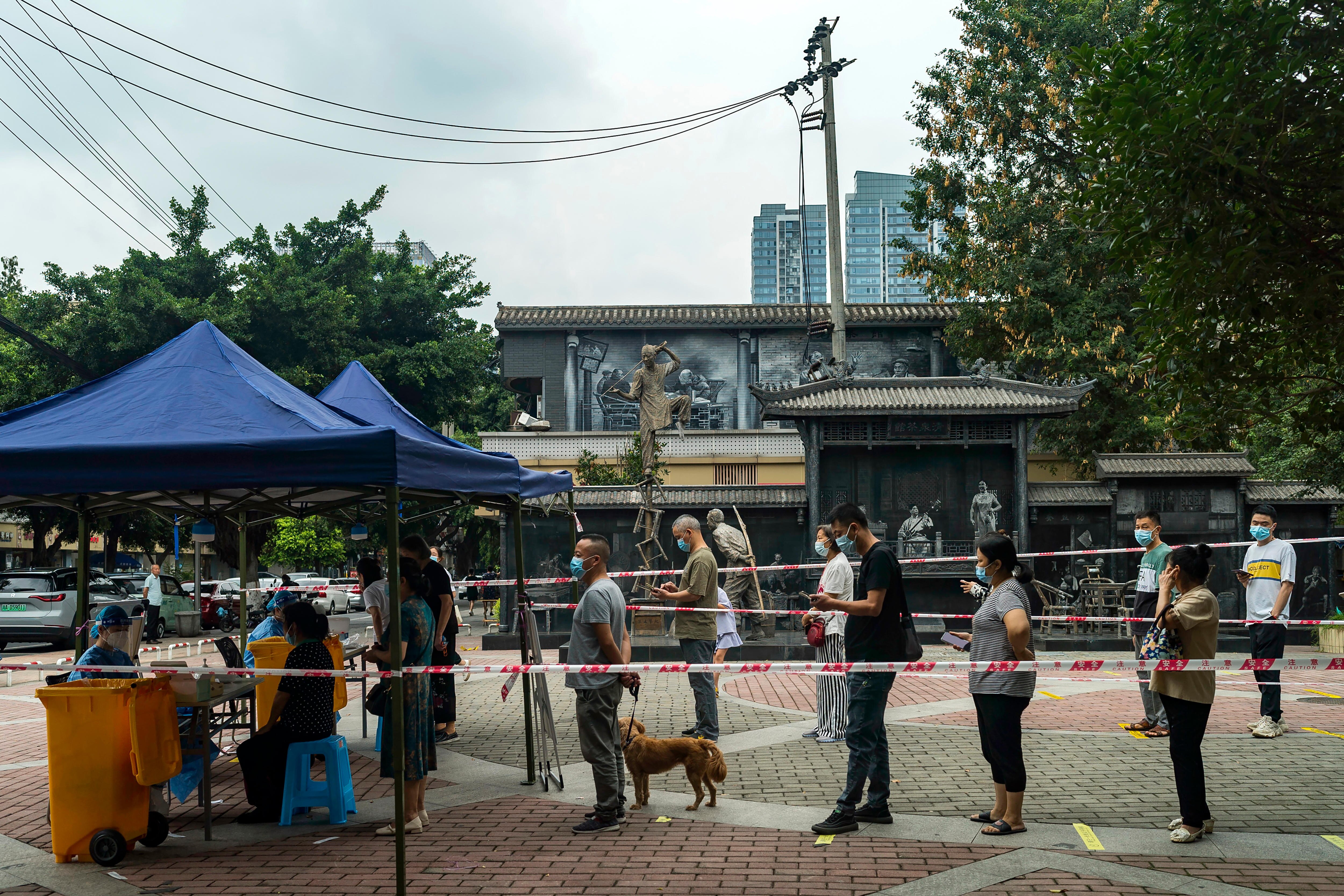 People wearing masks line up for COVID-19 testing in a paved courtyard.